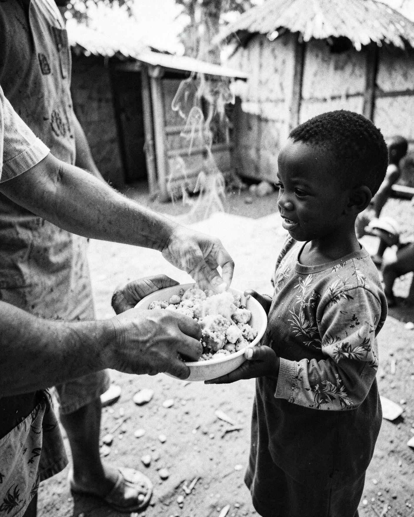 A young child in Africa receiving a bowl of hot food from a volunteer
